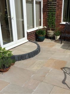 a patio with chairs and potted plants on the ground next to brick walls that have glass doors