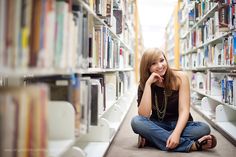 a woman sitting on the floor in front of bookshelves and smiling at the camera