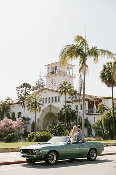 a bride and groom ride in the back of a green convertible car with palm trees