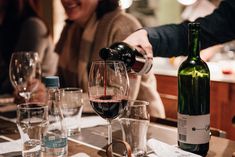 wine being poured into glasses on a table with people sitting at the bar in the background