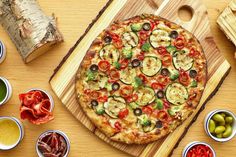 a pizza sitting on top of a wooden cutting board next to bowls of olives