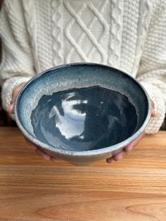 a person holding a bowl on top of a wooden table