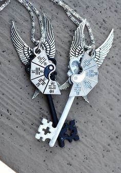 two necklaces with keys and wings are on the ground next to each other,