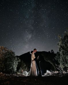 a bride and groom standing under the stars in the night sky