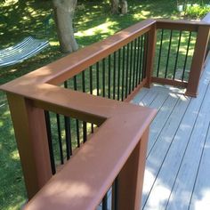 a wooden deck with metal railings next to a tree and grass covered park area