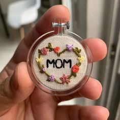 a hand holding a small embroidered badge with the word mom in it's center