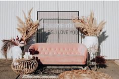 a pink couch sitting on top of a rug next to two vases filled with plants