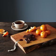 a wooden cutting board topped with oranges next to a cup of coffee