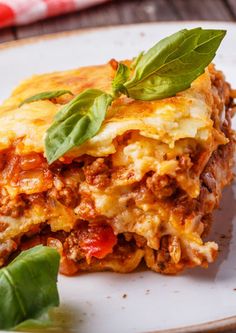 a white plate topped with lasagna covered in cheese and sauce, garnished with green leaves