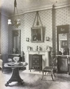 an old black and white photo of a living room with fireplace, chairs, mirror and table