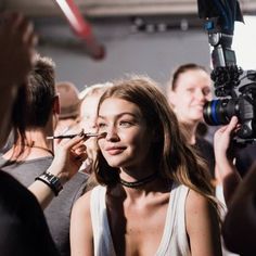 a woman getting her make up done by a cameraman in front of a group of people