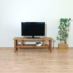 a television sitting on top of a wooden table next to a potted bamboo plant