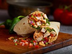 a burrito cut in half on top of a cutting board with chopped vegetables and salsa