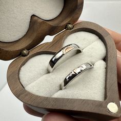 two wedding rings in a heart shaped box with white sand on the bottom and inside