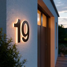 a house number sign on the side of a white building at night with light coming from it