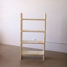 a wooden shelf sitting on top of a floor next to a white wall with a plant in it