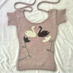 a sweater with swans on it is laying on a white sheet and there are two ties hanging from the shoulder