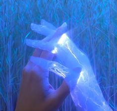 a hand is holding an ice - like object in front of some tall grass and blue lights