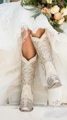 a woman in cowboy boots and wedding dress with flowers on her head is sitting down