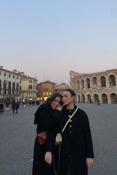 two people standing together in front of an old building with arches on the sides and cobblestone streets