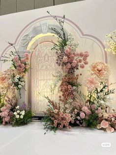 a white backdrop with pink flowers and greenery in front of an open door at night