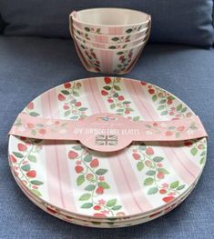 three plates and two cups sitting on a blue couch in front of a pillow with pink stripes