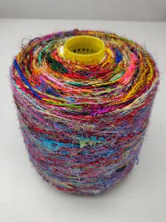 multicolored yarn spools are stacked on top of each other with a yellow cup in the middle