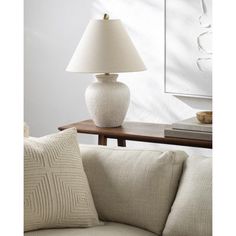 a white vase sitting on top of a couch next to a table with a lamp