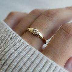 a woman's hand wearing a gold ring with a diamond on the middle finger