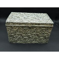 a silver box sitting on top of a black surface with an intricate design in the middle