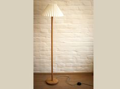 a wooden floor lamp with a white shade on it's base and a black cord plugged in