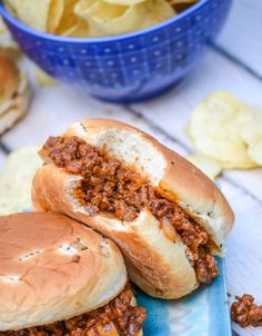 two sloppy joe sandwiches sitting on top of a blue plate next to some potato chips