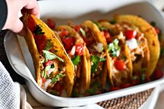 a person is picking up some tacos out of a dish with tomatoes and cilantro