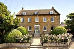 a large brick house with lots of windows and bushes around the front door, on a sunny day