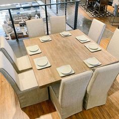 a wooden table with white plates and placemats on it in a large room