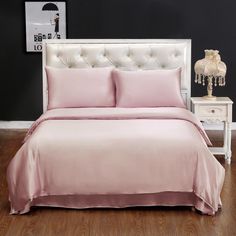 a bed with a pink comforter and pillows on top of it next to a night stand