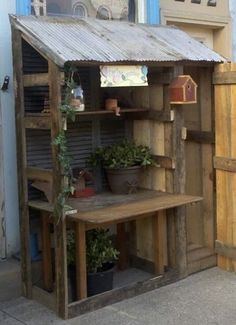 an old wooden shed with potted plants on the outside and shelves in front of it