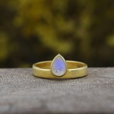 a yellow gold ring with a blue tear shaped stone on the outside, sitting on top of a rock