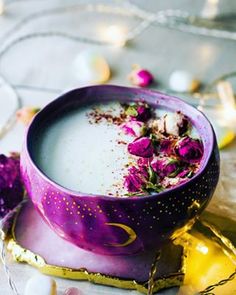 a purple bowl filled with white liquid and pink flowers on top of a table next to gold foil