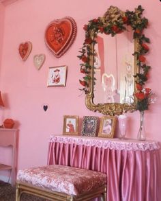 a room with pink walls and pictures on the wall, including a mirror above a bench