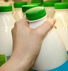 a hand is holding a plastic bottle in front of several milk bottles with green caps