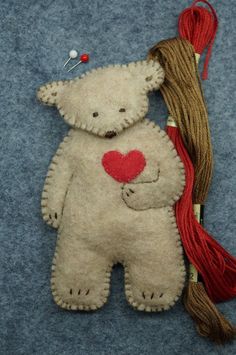 a white teddy bear with a red heart on it's back and some thread