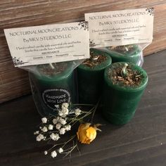 three green candles sitting next to each other on top of a wooden table with white flowers