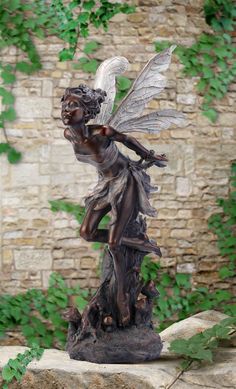 a statue of a fairy on a rock in front of a brick wall with ivy growing around it