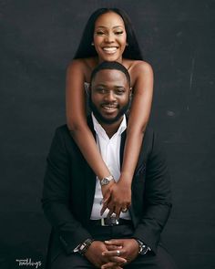 a man and woman sitting on top of each other in front of a black background