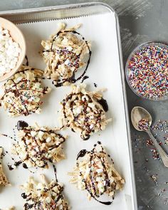 sprinkle covered cookies on a baking sheet with spoons and bowl of sprinkles