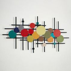 a wall sculpture made out of different colored circles on black metal rods with white walls in the background