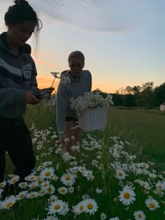 two girls in a field with daisies and one girl holding a basket full of daisies