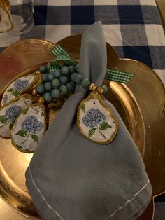 a gold plate with blue and white napkins on it next to a glass vase