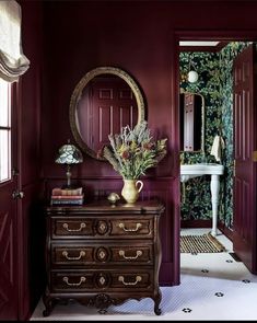 a room with red walls and a dresser in the corner, along with a mirror